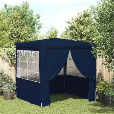 A dark blue party tent set up on a grassy lawn, surrounded by trees and a wooden fence.