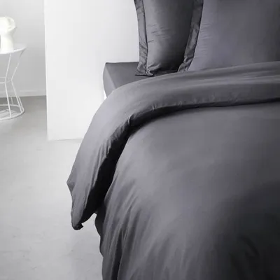 A close-up view of a dark grey duvet cover on a bed, with pillows visible in the background.