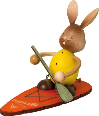 A wooden figurine of a rabbit on a surfboard with a paddle.
