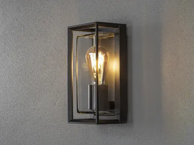A black outdoor wall light with a clear glass enclosure and an exposed filament bulb is mounted on a textured gray wall.