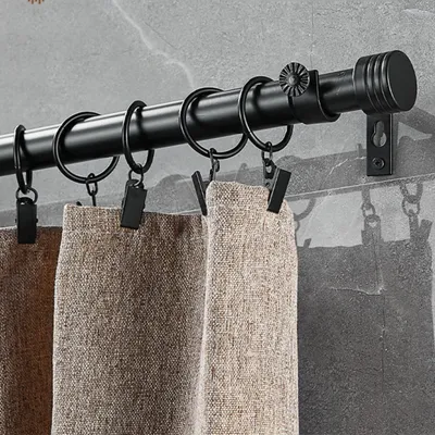 A close-up view of a black curtain rod with rings and clips holding up beige curtains against a gray tiled wall.