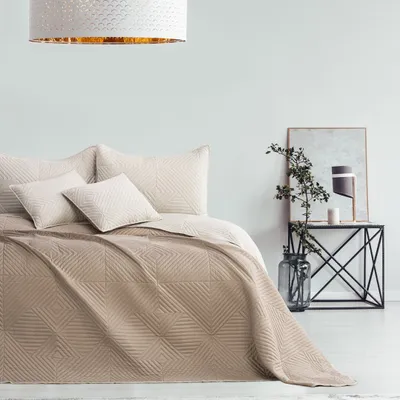 A bed with a quilted throw and pillows, next to a side table with a lamp and plant.