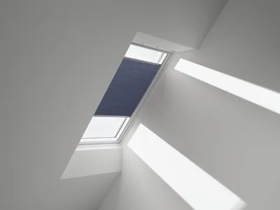 A skylight with a blue pleated blind partially covering it, with sunlight casting shadows on the surrounding walls.