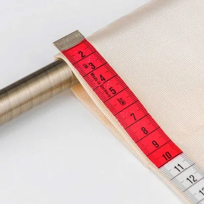 A close-up of a beige fabric being measured by a red tape measure.