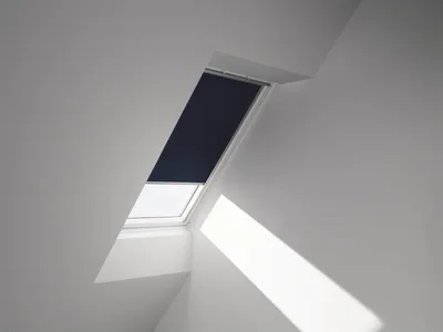 A skylight window with a dark blue roller blind partially drawn, showing a beam of light entering the room.