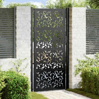 A black metal garden gate with a leaf design, set in a garden with brick pillars and greenery.