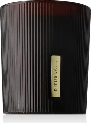 A close-up studio shot of a scented candle in a dark, ribbed glass jar with a gold label.