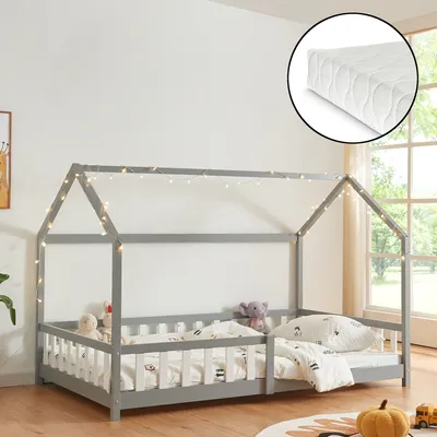 A child's house bed with a mattress and fairy lights, set in a room with a window.