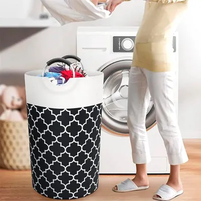 A person is putting laundry into a fabric hamper next to a washing machine.