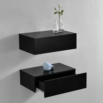 Two black floating shelves mounted on a light gray wall. The top shelf holds two clear glass vases, one with a white rose. The bottom shelf has a light blue decorative object and its drawer is partially open.