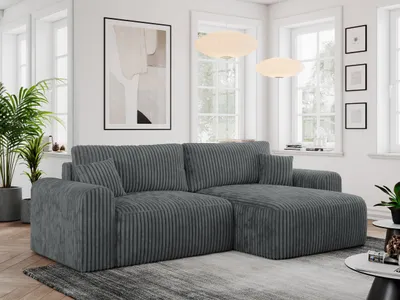 A modern living room with a large, dark gray corduroy sectional sofa as the main focus. The sofa is placed on a rug in front of a window with natural light. Decorative elements like plants and artwork are visible.