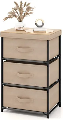A beige fabric dresser with three drawers and a black metal frame, decorated with a vase of dried flowers and a decorative ring on top.