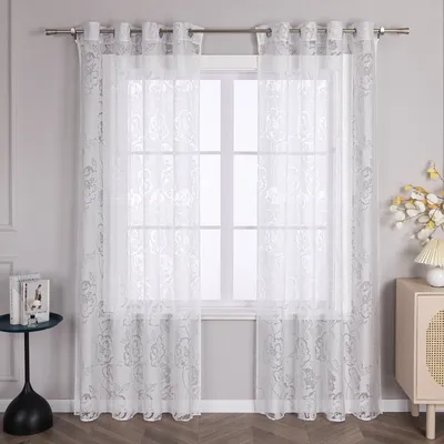 A window with white lace curtains with a floral pattern.