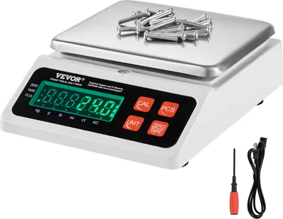 A digital scale with a stainless steel platform and a white base, displaying a green LED screen. Several metal fasteners are placed on the platform. A screwdriver and a power cord are visible to the right of the scale.