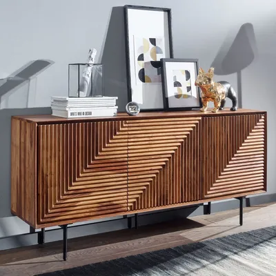 A wooden sideboard with decorative carvings, displayed in a room setting with framed art and decorative objects.
