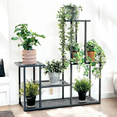 A multi-tiered metal plant stand filled with various potted plants, placed indoors against a white wall.