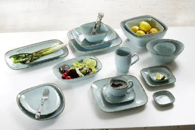 A collection of blue ceramic tableware, including plates, bowls, and a mug, arranged on a white surface.