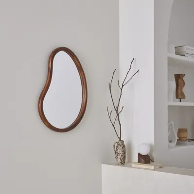 A modern living room corner with a mirror, vase with branches, and a lamp on a shelf.