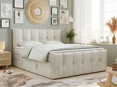 A bedroom scene with a beige boxspring bed as the focal point, decorated with artwork and plants.