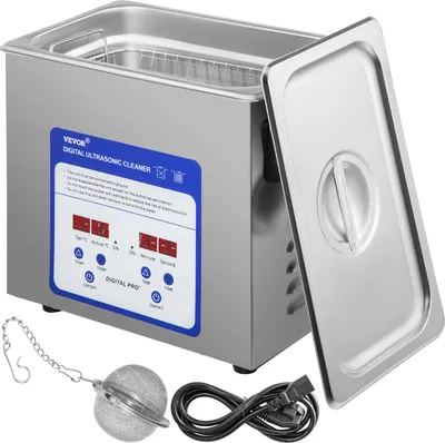 A stainless steel ultrasonic cleaner with its lid open, along with accessories like a mesh basket, a tea strainer, and a power cord.