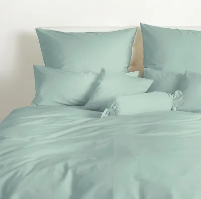 A neatly made bed with light green bedding, including pillows and a bolster pillow.