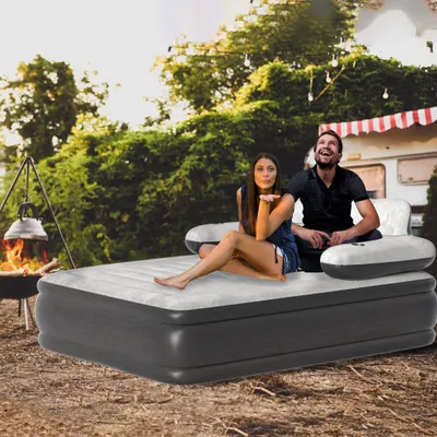 A couple relaxing on an inflatable mattress outdoors with a campfire and a camper van in the background.