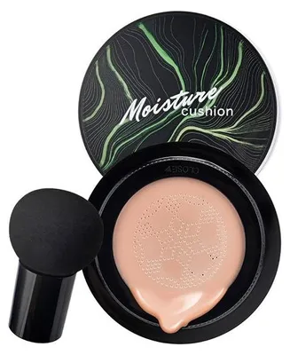 Schwarzes Cushion-Foundation-Kompakt mit grünem Blattdesign auf dem Deckel, geöffnet, um ein helles Pfirsich-Foundation und einen schwarzen pilzförmigen Make-up-Schwamm zu zeigen