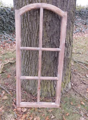 A wooden window frame leaning against a tree trunk outdoors.