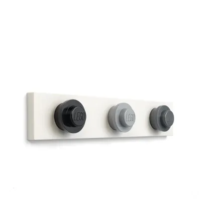 A white wall with a white shelf holding three LEGO brick-shaped coat hooks in black, light gray, and dark gray.