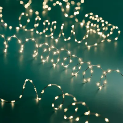 Three strands of warm white LED string lights coiled on a teal background.