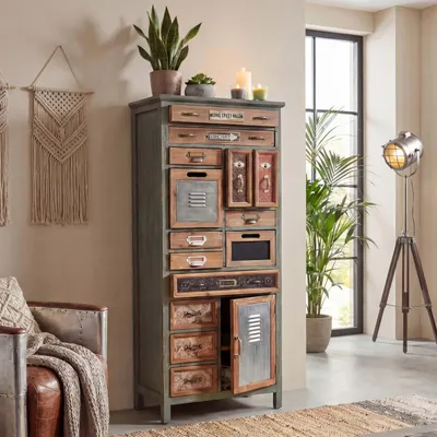 A vintage-style apothecary cabinet filled with drawers and a cabinet door, placed in a room setting with a chair and a floor lamp.