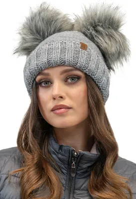A woman wearing a gray knitted winter hat with two faux fur pom-poms.