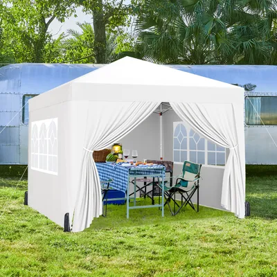 A white pop-up canopy tent set up on grass next to a vintage trailer, with a table and chairs inside.