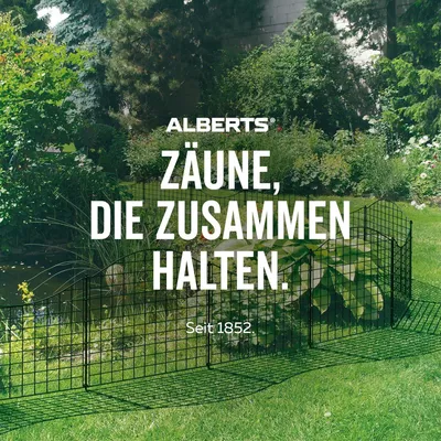 A black wire fence is set up in a lush green garden with a pond in the background.