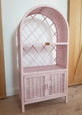A pink wicker bookshelf with two doors at the bottom is shown against a neutral background.