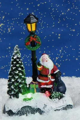Der Weihnachtsmann, der in einer verschneiten Landschaft neben einer Laterne mit einem Kranz steht.