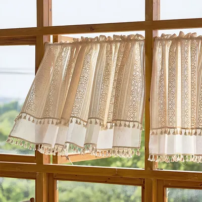 Two cafe curtains with tassels hanging in a wooden window frame, with greenery visible outside.