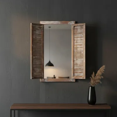 A mirror with shutter-style side panels is mounted on a dark gray wall above a wooden console table. A black vase with dried grass is on the table.