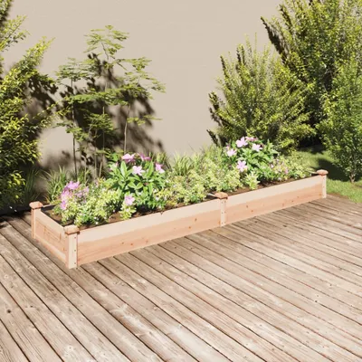 Two wooden raised garden beds filled with plants and flowers are placed on a wooden deck in front of a wall.