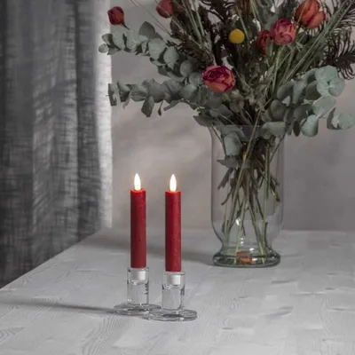Two red LED candles in glass holders on a table with a bouquet of dried flowers in the background.