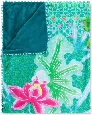 A folded blanket with a floral and leaf pattern on one side and a solid teal color on the other, trimmed with small pom-poms.