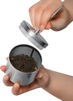 Hands holding a stainless steel tea infuser filled with loose leaf tea, with the lid being held above it.