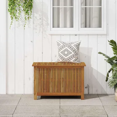A wooden storage box with a pillow on top, placed on a tiled patio in front of a white wooden wall with a window.