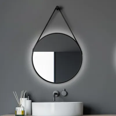 A round LED mirror with a black frame and a leather-look strap is mounted on a gray wall above a white sink.