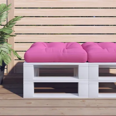 A pink cushion on a white pallet bench on a wooden deck.
