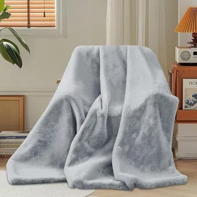 A light gray plush blanket is draped over a chair in a room with blinds and a plant.