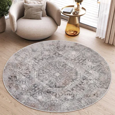 A round rug with a vintage pattern is placed on a wooden floor in a living room setting, next to a chair and a side table.