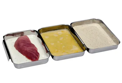 Three stainless steel trays are arranged side-by-side, with a piece of raw meat in the first tray, a beaten egg mixture in the second, and breadcrumbs in the third.