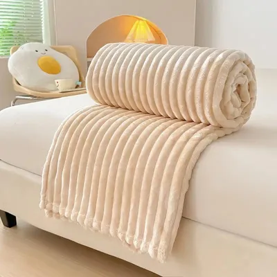 A rolled-up beige blanket is placed on a white surface, possibly a bed or sofa. A pillow shaped like a fried egg is visible in the background.