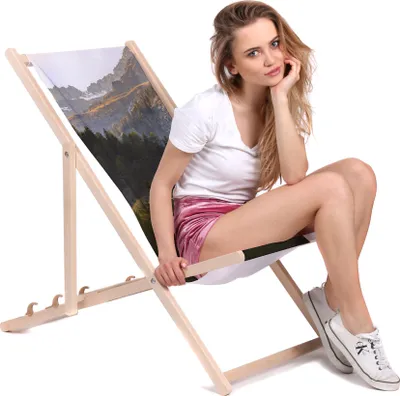 A young woman is sitting on a foldable deck chair with a mountain landscape printed on the fabric.